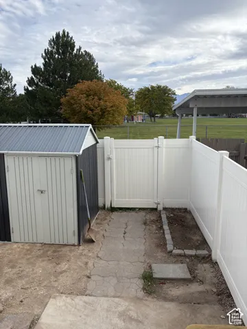 Exterior storage shed with a metal roof, white vinyl privacy fencing, pedestrian gate, and stone-bordered garden bed