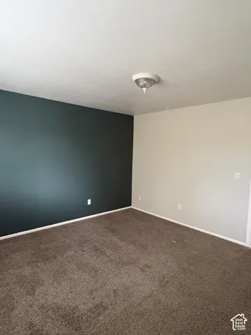 Room featuring high-contrast dark teal and neutral wall paint, neutral carpeting, and a central flush-mount ceiling light fixture