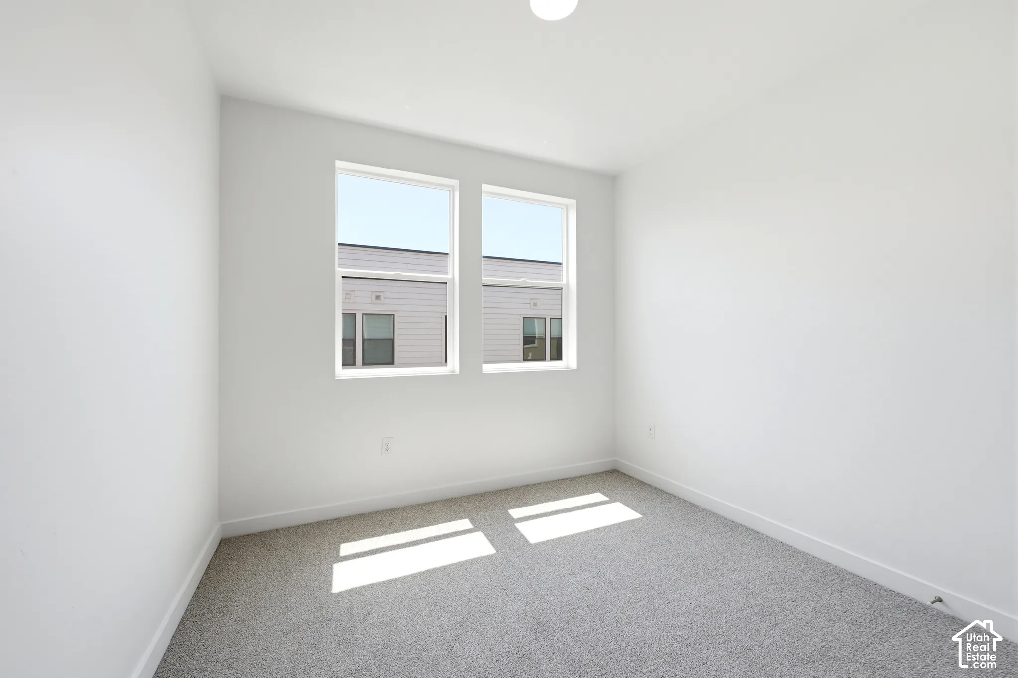 Neutral interior featuring high-pile wall-to-wall carpeting, white walls, dual windows with white frames, and a recessed ceiling light fixture