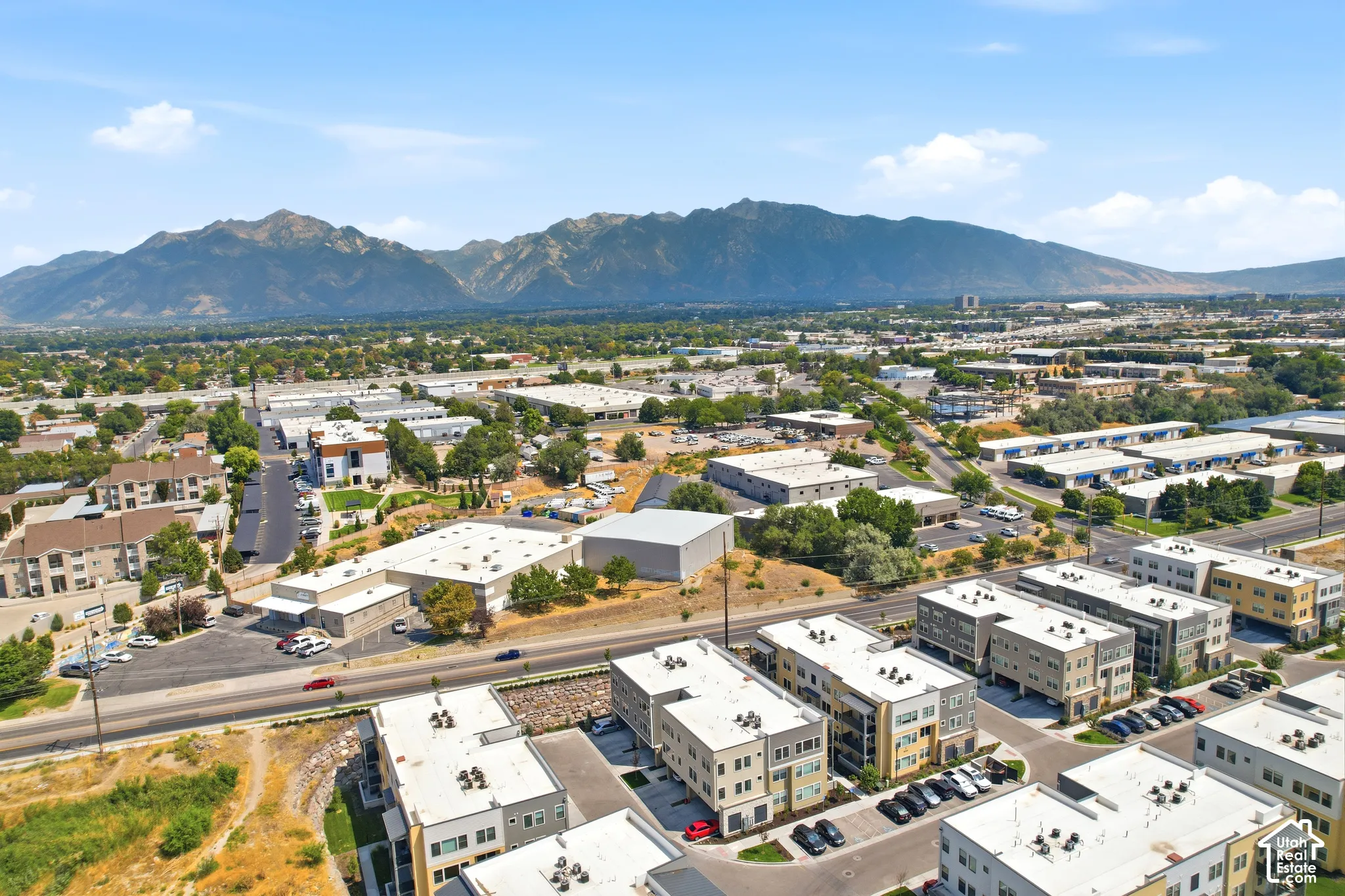 Aerial perspective featuring multi-story residential buildings, paved surface parking, and a prominent mountain range backdrop