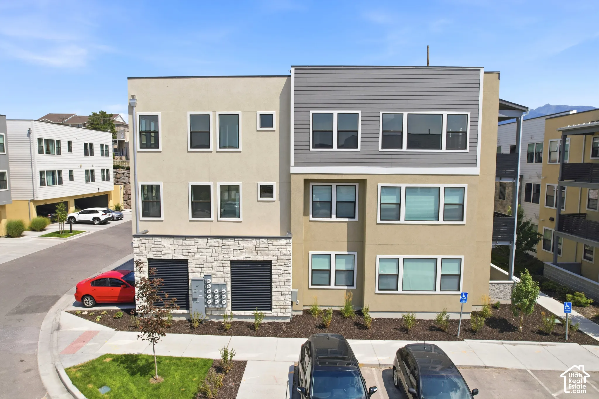 Contemporary multi-level building exterior featuring a mix of stucco and horizontal siding, stone veneer base, and large rectangular window configurations