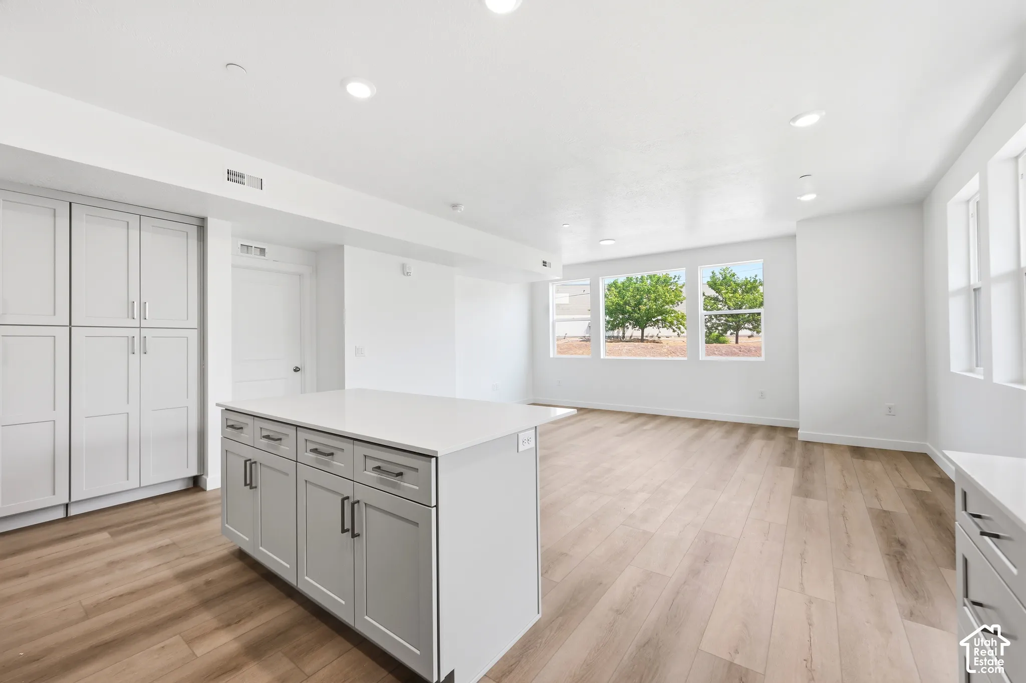 Neutral-toned cabinetry, solid surface island countertop, recessed ceiling lighting, and wood-finish flooring