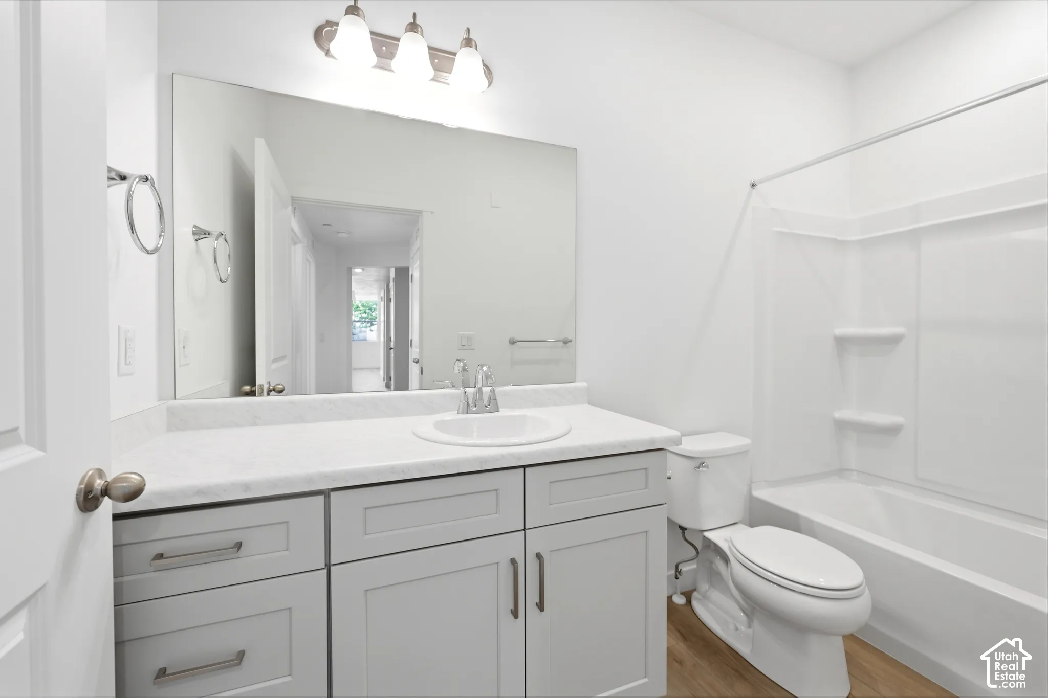 Bathroom featuring a gray vanity with an integrated basin, stone-composite countertop, full-width vanity mirror, three-light fixture, and a tub-shower combination with built-in shelving
