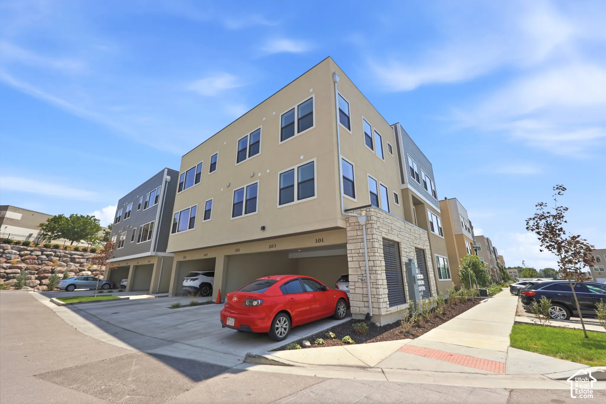 Modern multi-story exterior featuring a stucco facade, stacked stone accents, and integrated covered parking
