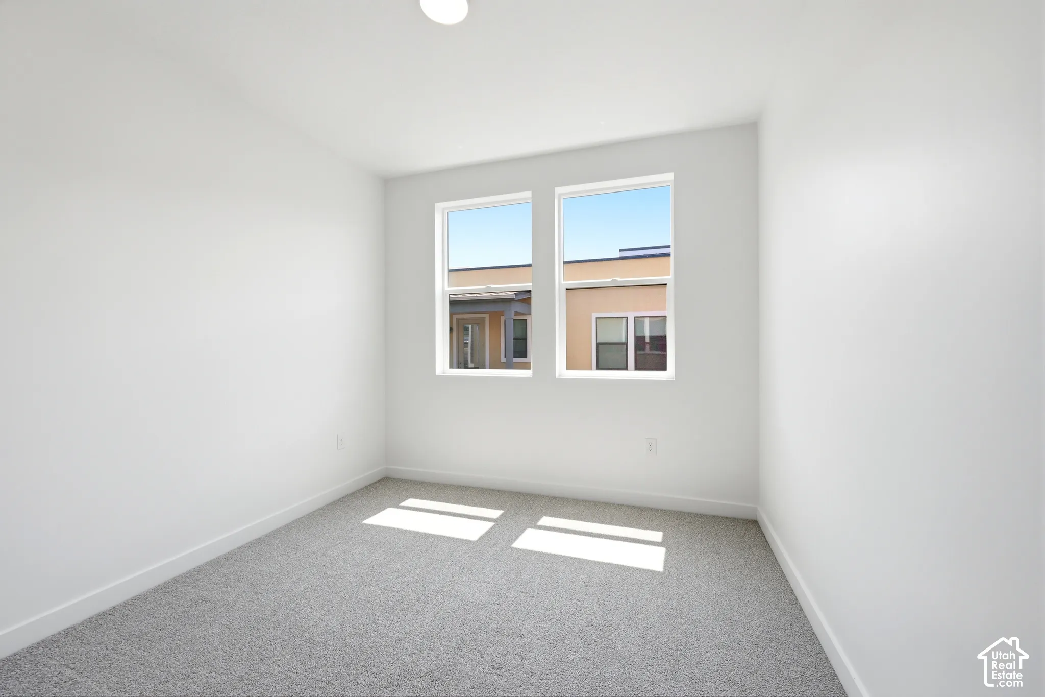Neutral-toned interior space featuring light-colored wall paint, plush carpeting, and two dual-pane windows with white frames