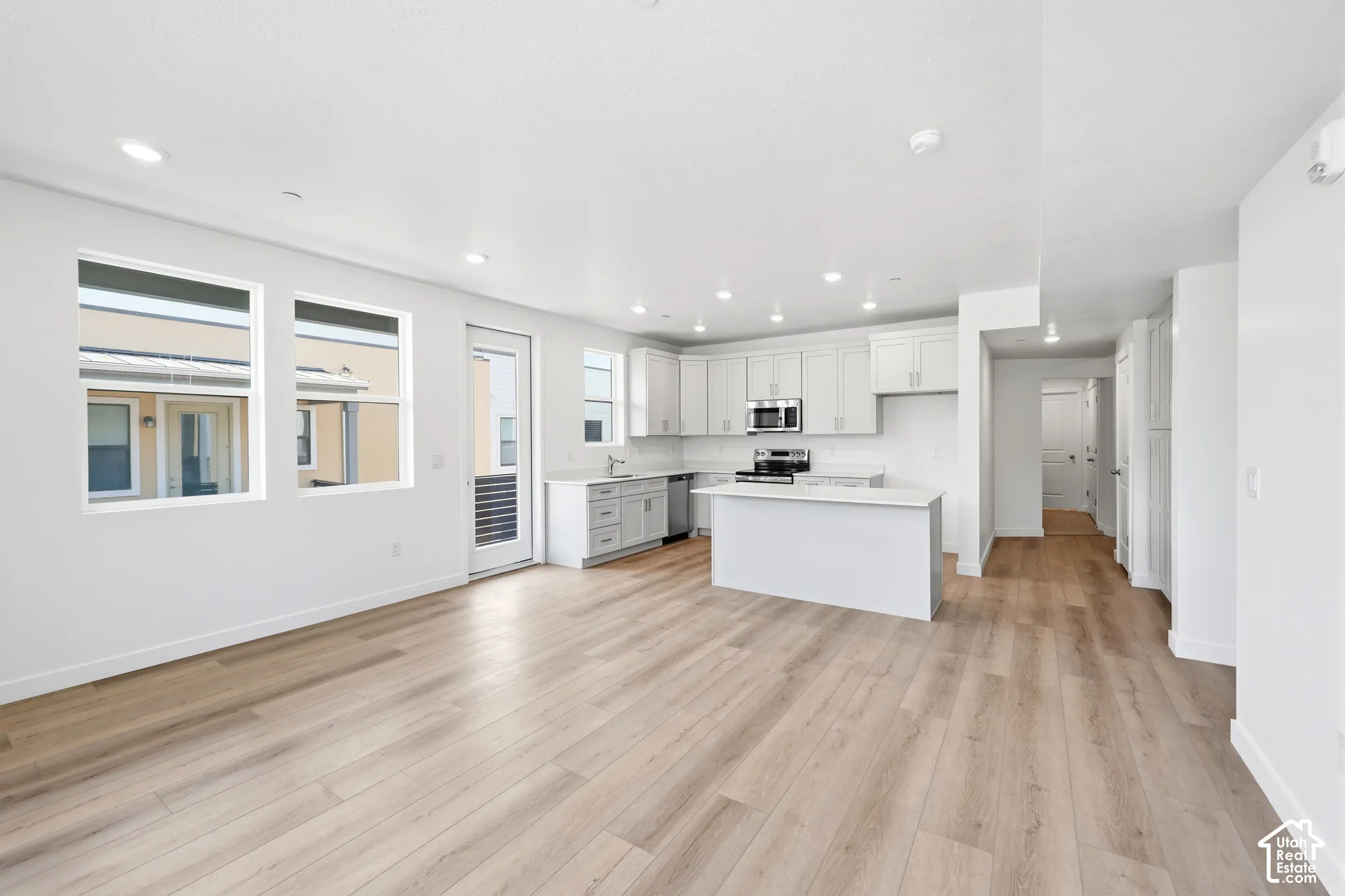 Kitchen featuring white cabinetry, solid-surface countertops, stainless steel appliances, recessed lighting, and wood-finish flooring