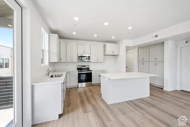 Kitchen featuring white shaker-style cabinetry, a central island with a quartz countertop, stainless steel appliances, and wood-finish flooring