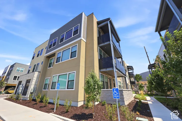 Contemporary multi-story exterior featuring a mix of stucco and horizontal panel siding, stone veneer accents, large rectangular windows, and private balconies with dark metal railings