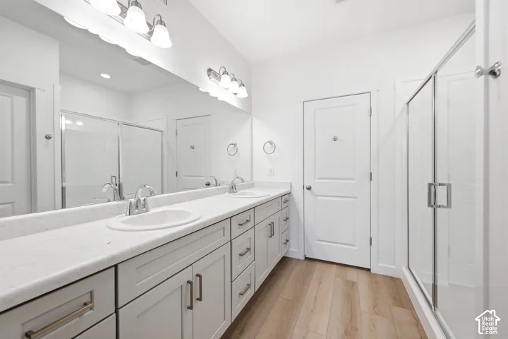 Dual-vanity cabinetry with light-toned countertops, full-width vanity mirror, walk-in shower with glass enclosure, and wood-finish flooring