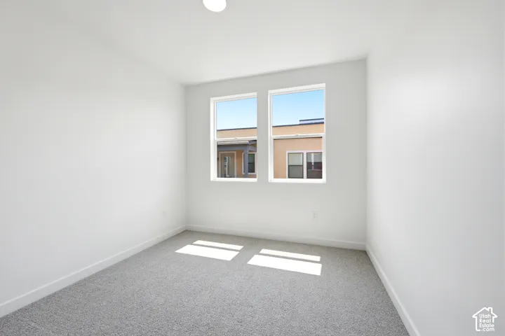 Neutral-toned interior space featuring light-colored wall paint, plush carpeting, and two dual-pane windows with white frames