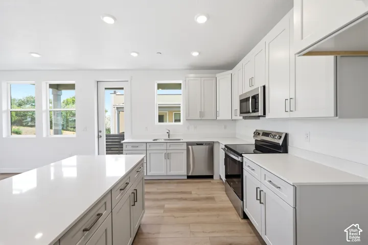 Kitchen featuring white shaker cabinetry, quartz countertops, a central island, wood-finish flooring, and stainless steel appliances