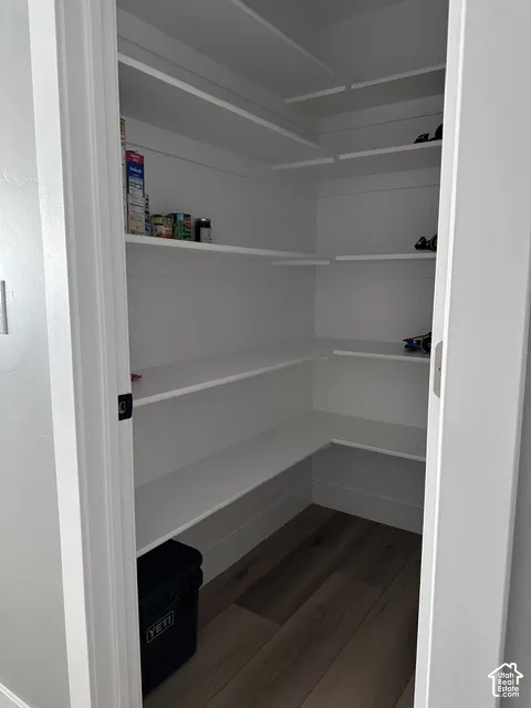 Walk-in pantry featuring white wrap-around shelving and wood-finish flooring