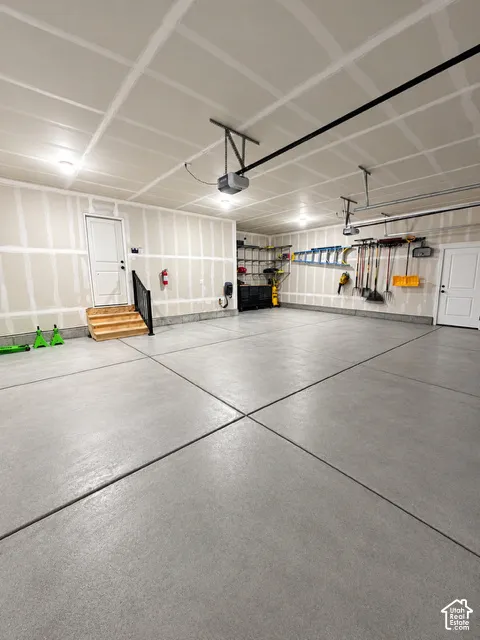 Multi-car garage featuring a sealed concrete floor, drywall finish, overhead door openers, and integrated wooden staircase with metal handrail