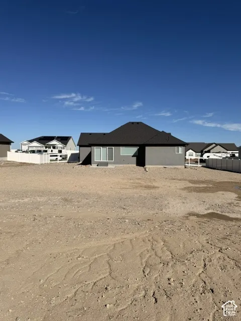 Exterior rear elevation featuring dark grey stucco siding, a hipped roof with asphalt shingles, sliding glass patio doors, and white vinyl privacy fencing