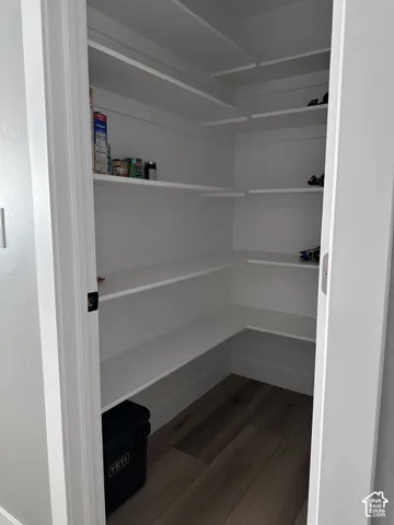 Walk-in pantry featuring white wrap-around shelving and wood-finish flooring