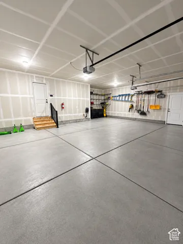 Multi-car garage featuring a sealed concrete floor, drywall finish, overhead door openers, and integrated wooden staircase with metal handrail