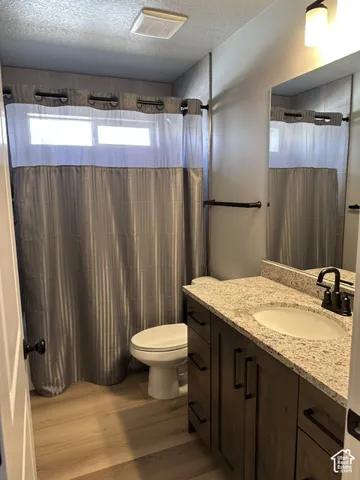 Bathroom featuring wood-finish flooring, a vanity with stone-composite countertop, an integrated sink, matte black hardware, and an oversized wall-mounted mirror