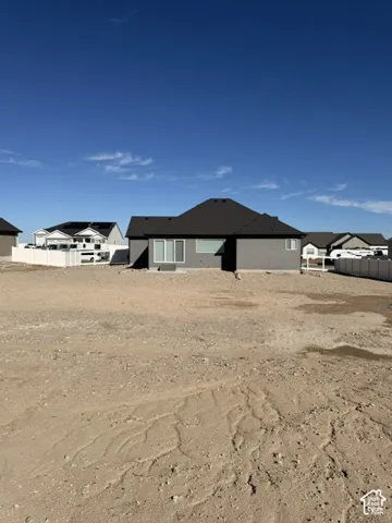 Exterior rear elevation featuring dark grey stucco siding, a hipped roof with asphalt shingles, sliding glass patio doors, and white vinyl privacy fencing