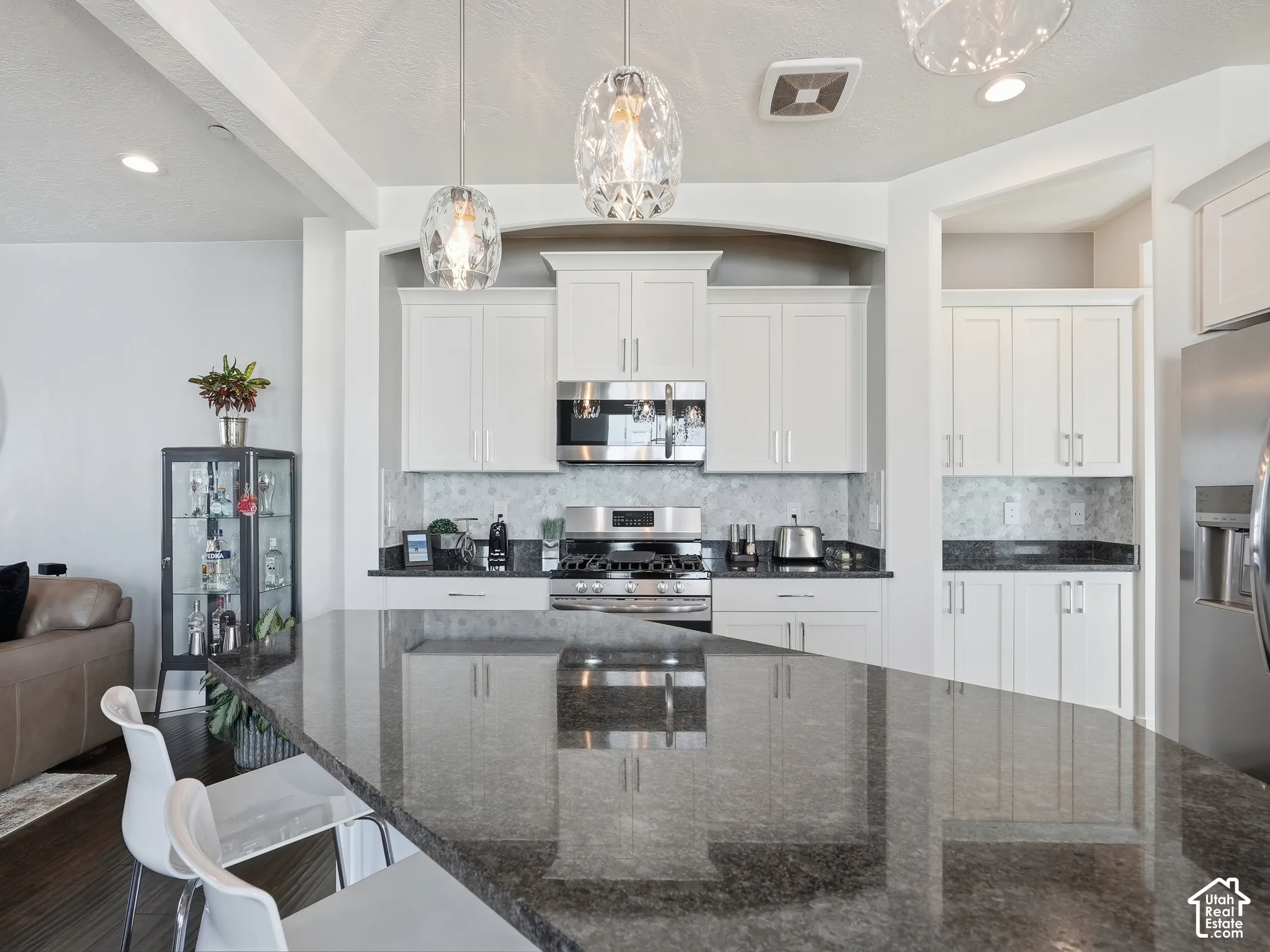 Kitchen featuring white cabinetry, dark stone countertops, stainless steel appliances, a tiled backsplash, and decorative pendant lighting