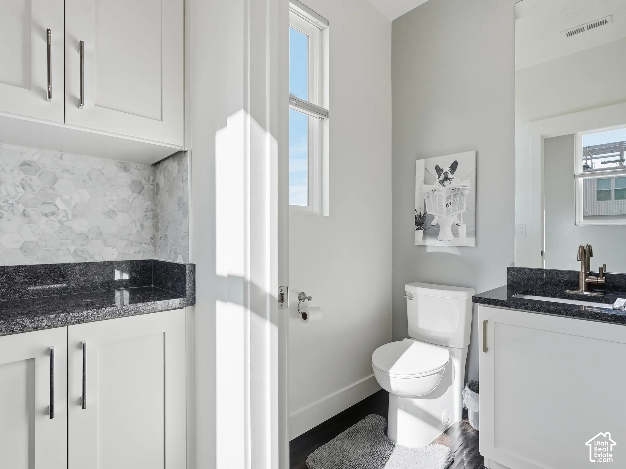 Bathroom featuring white cabinetry, dark stone countertops, a hexagonal tile backsplash, and a wall-mounted faucet
