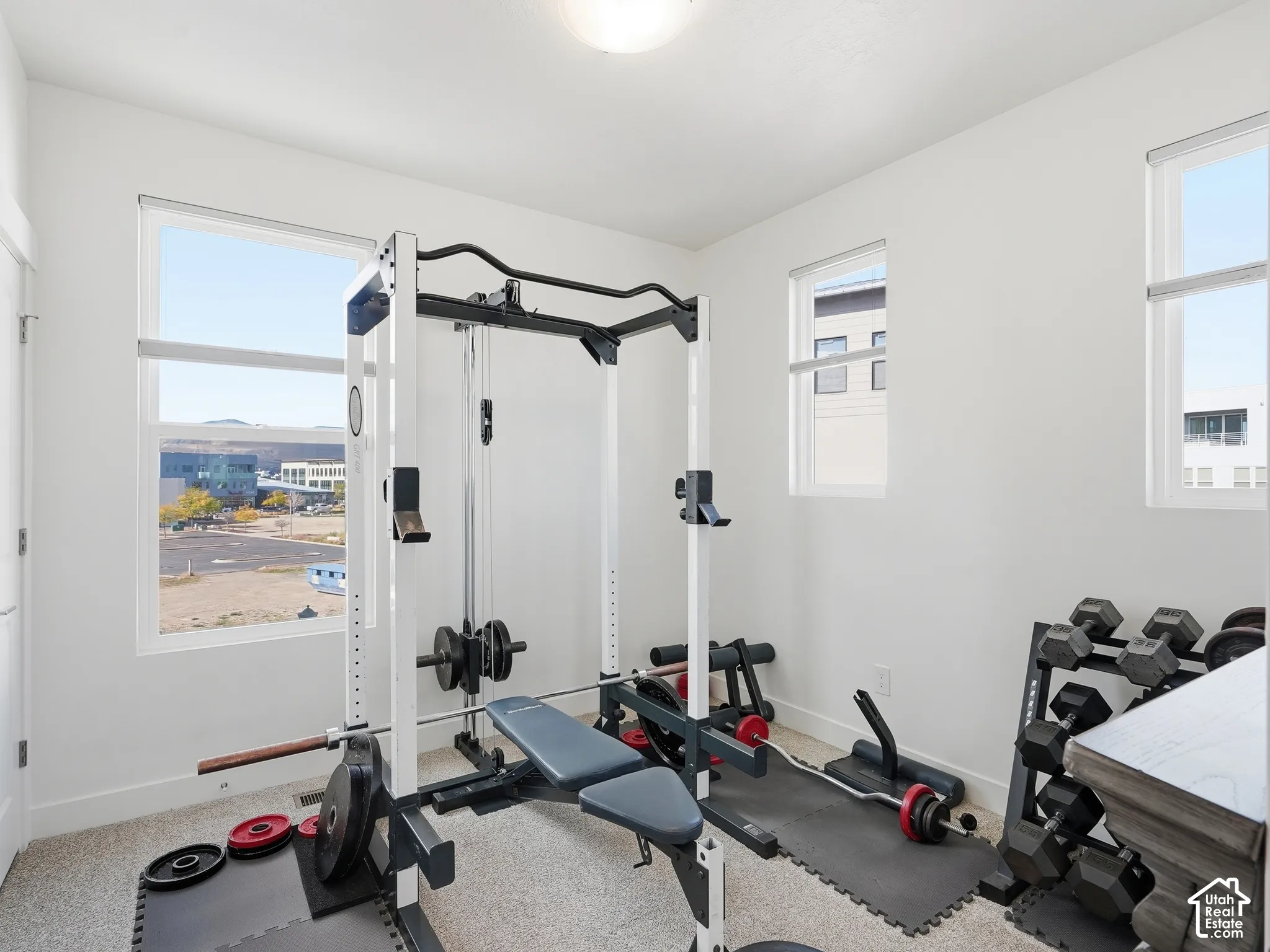 Neutral-toned room featuring light carpeting, crisp white walls, and triple windows providing natural illumination