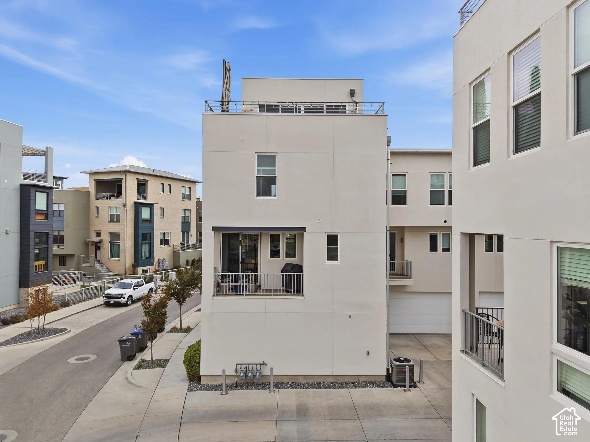 Modern multi-story exterior with a flat roof, integrated balcony, stucco finish, and rooftop railing