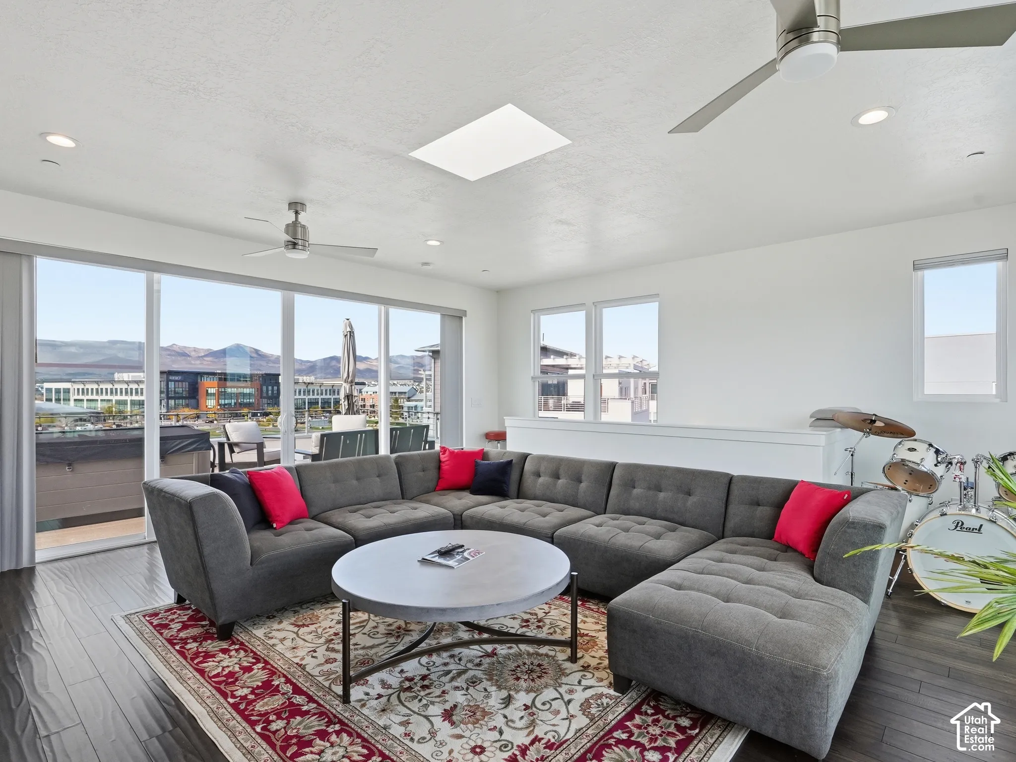 Living area featuring wood-finish flooring, a ceiling-mounted skylight, recessed lighting, dual ceiling fans, and expansive floor-to-ceiling glass sliding doors