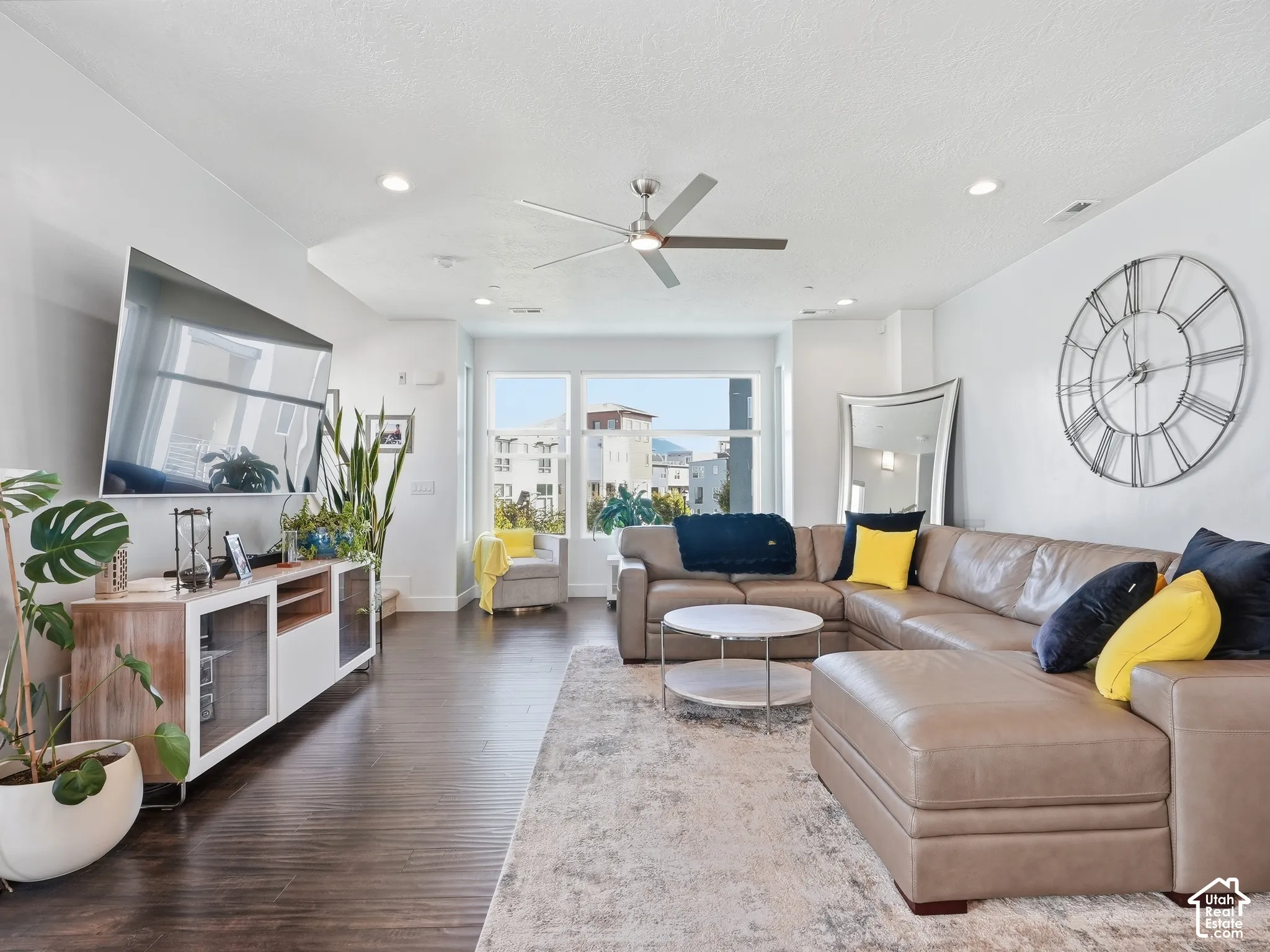 Living area featuring dark wood-finish flooring, recessed lighting, a modern ceiling fan, and large windows