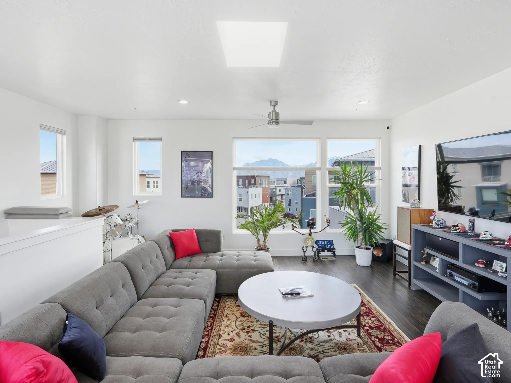 Living area featuring dark wood-finish flooring, a ceiling-mounted fan, a square skylight, and large picture windows framing mountain scenery