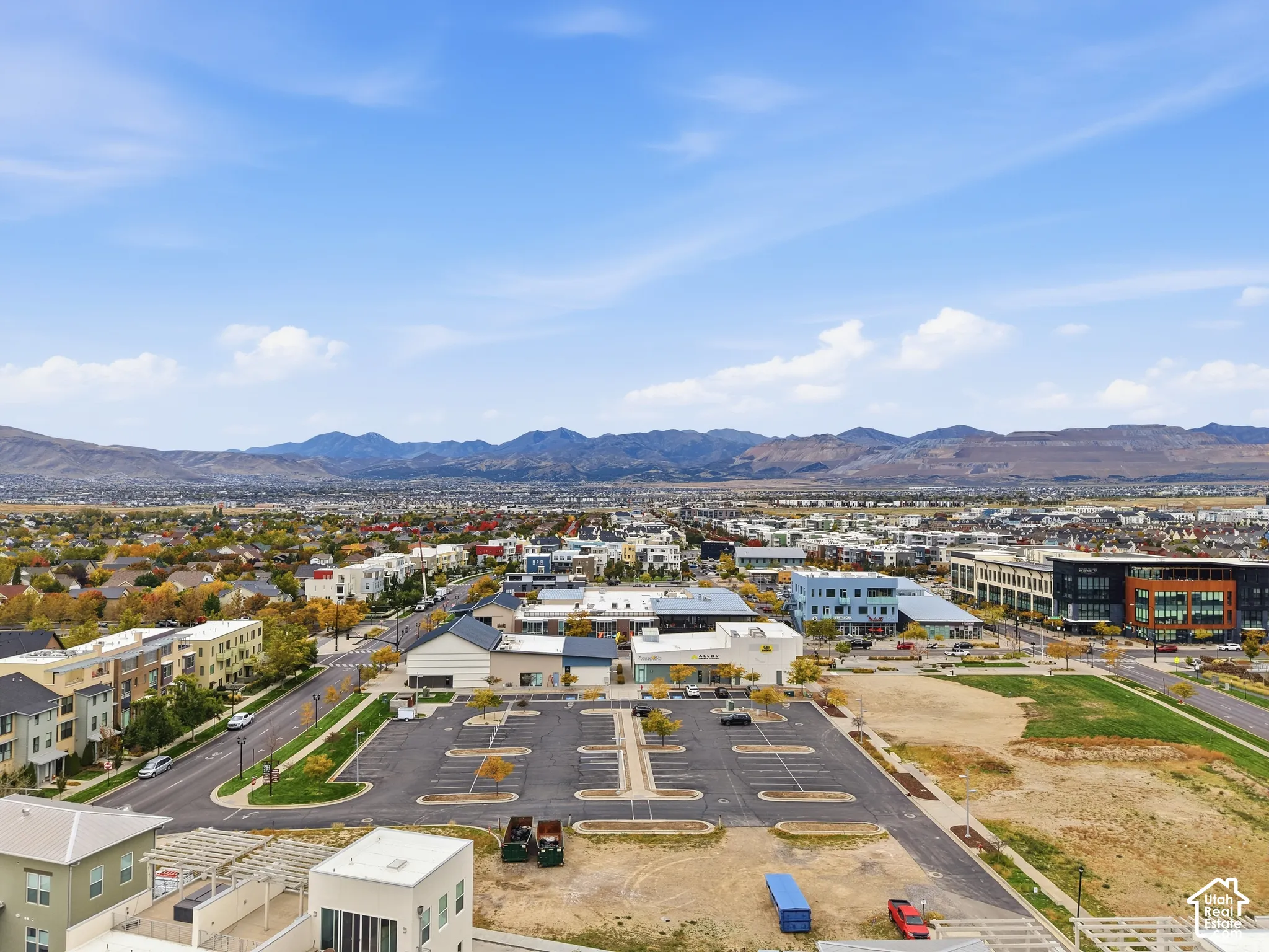 Aerial perspective of the property surroundings featuring paved parking infrastructure, paved thoroughfares, mature trees, and a mountain range backdrop