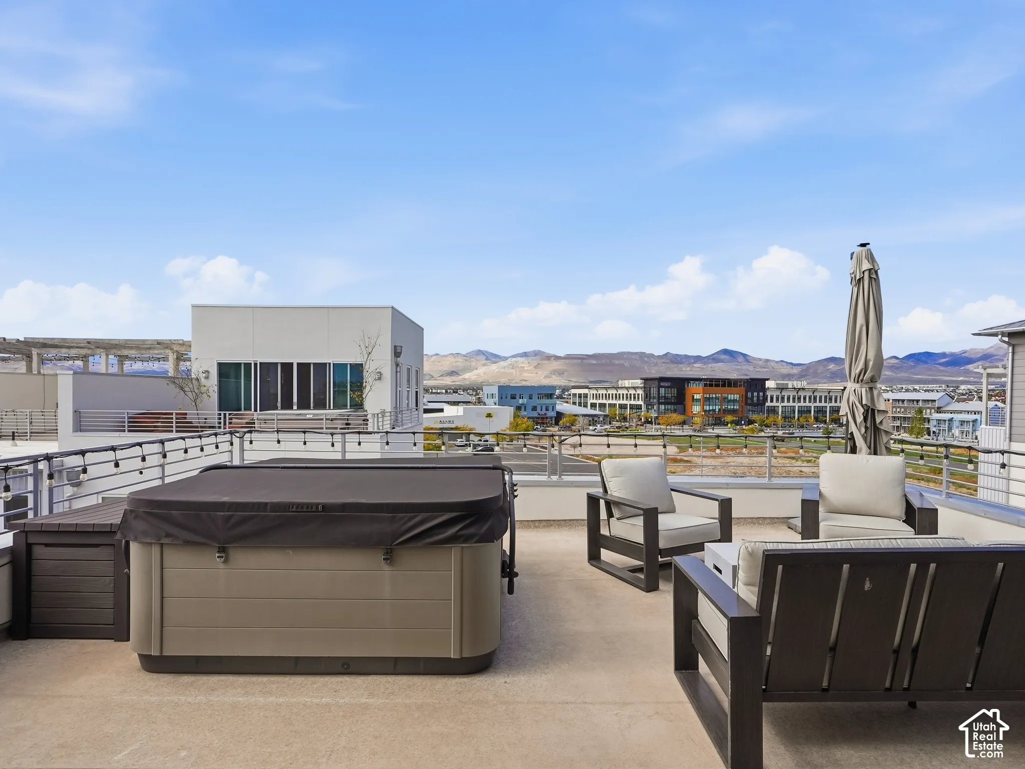 Expansive rooftop terrace featuring a hardscaped deck, perimeter metal railing with integrated string lighting, and panoramic mountain backdrop
