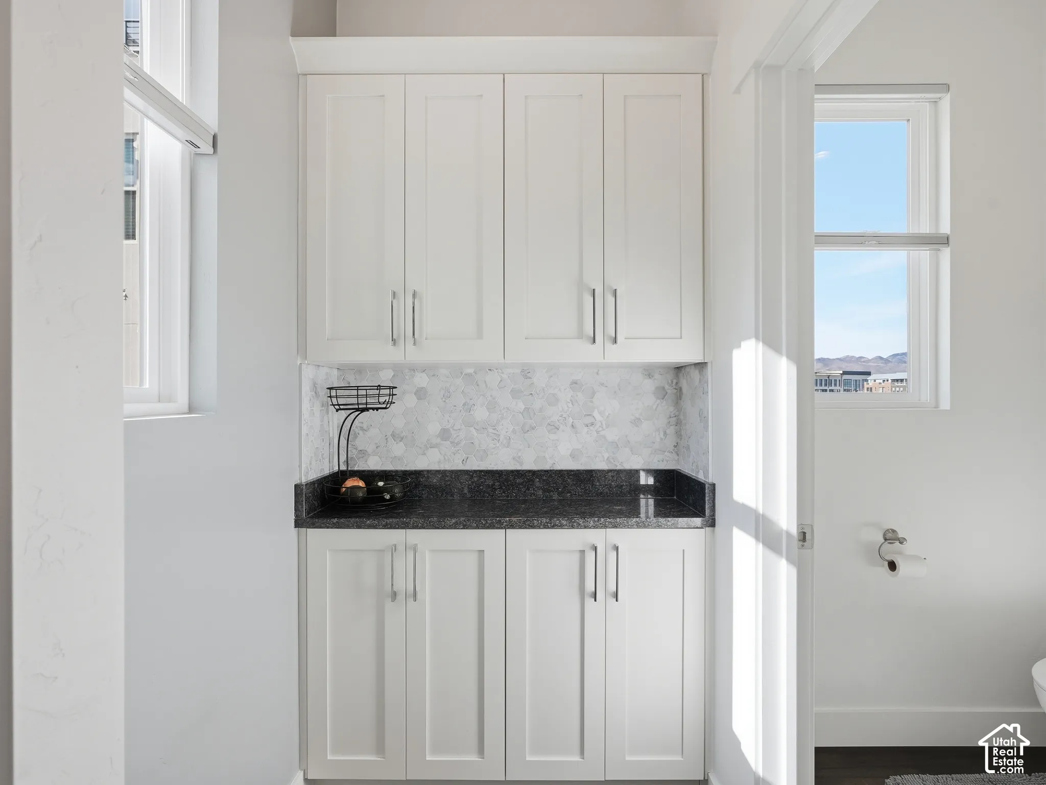 Custom cabinetry featuring Shaker-style doors and metallic hardware, dark stone countertop, and hexagonal mosaic tile backsplash