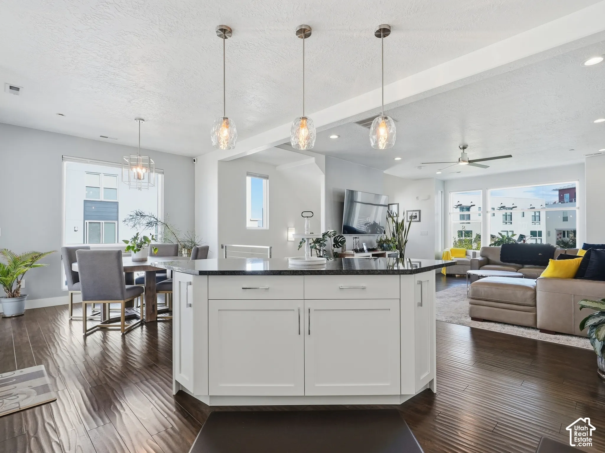 Kitchen island with white shaker-style cabinetry, dark stone countertop, three brushed-nickel glass pendant lights, and wood-finish flooring