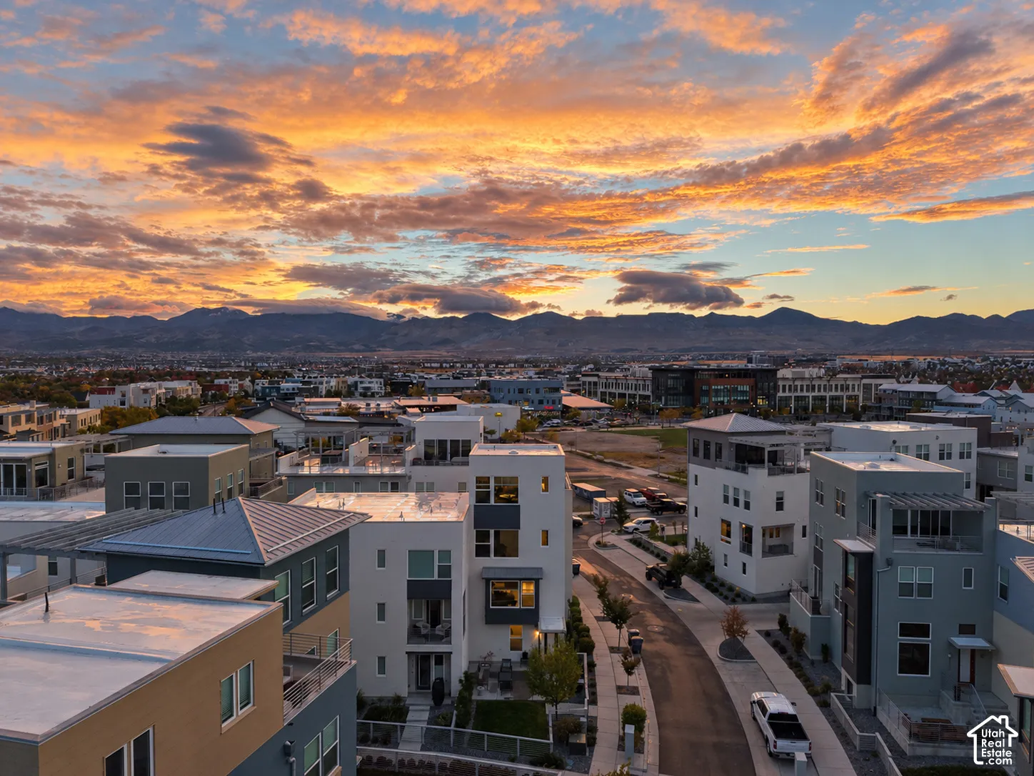 Aerial perspective featuring multi-story contemporary structures, flat rooflines, paved street infrastructure, and a mountain range backdrop