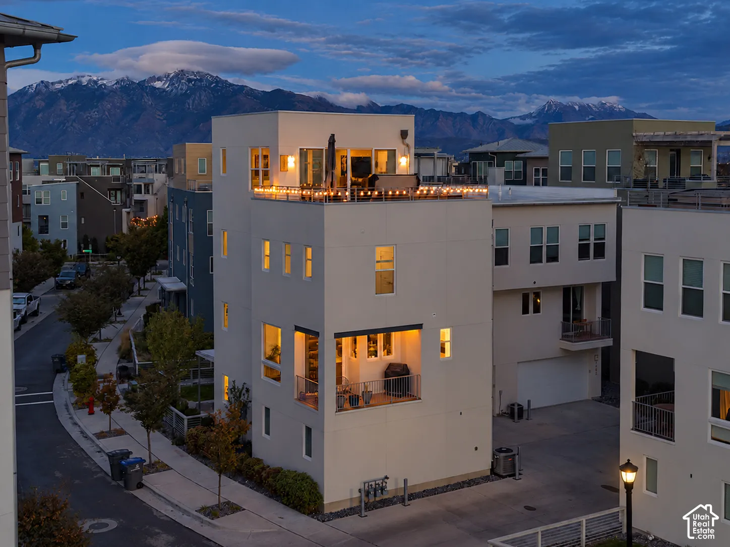 Multi-level modern exterior featuring a rooftop deck, an integrated covered balcony, metal railings, and mountain backdrop