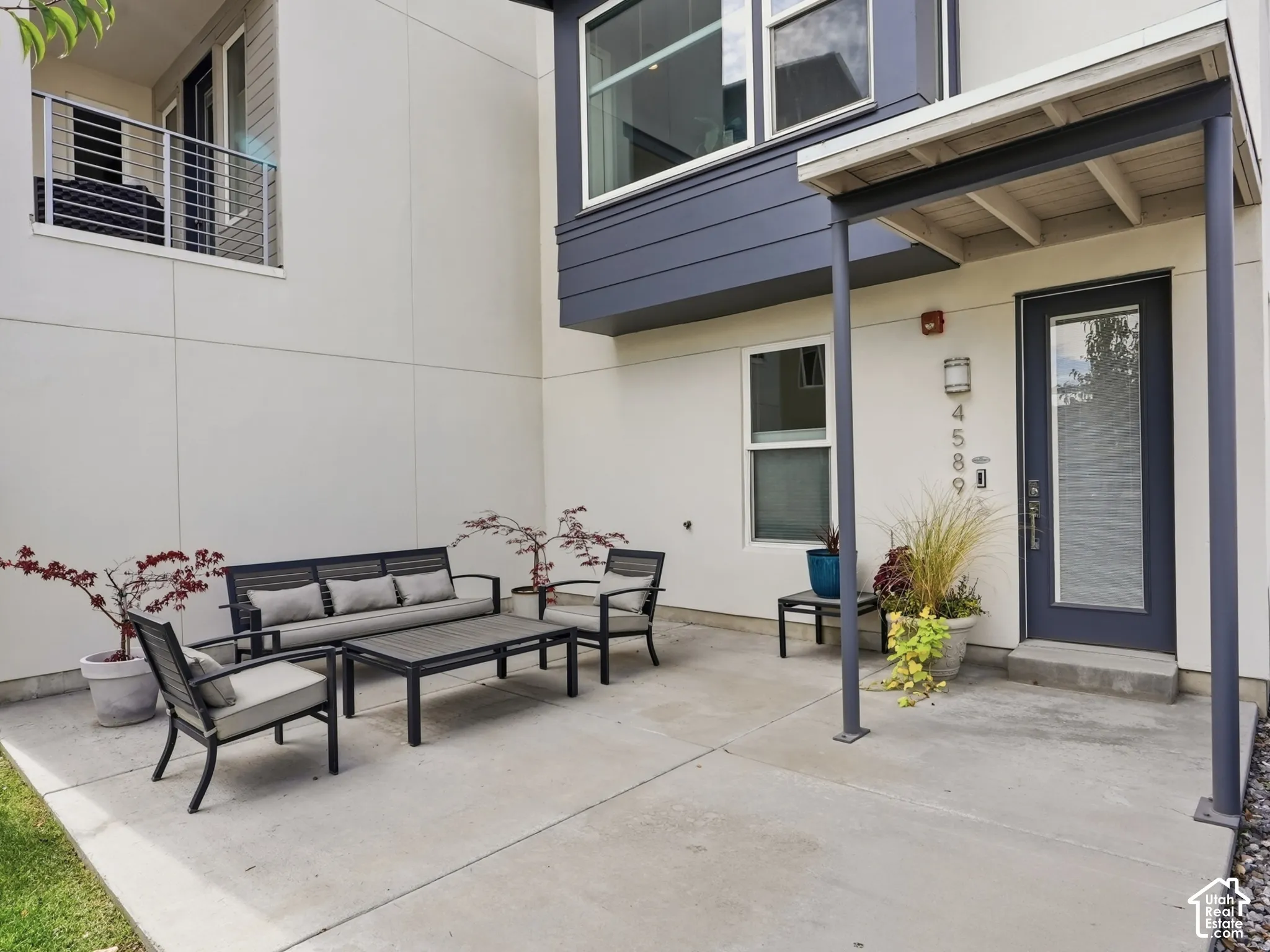 Concrete patio with a covered entrance featuring a steel-frame canopy, exterior metal sconce lighting, and a metal-trimmed glass-panel door