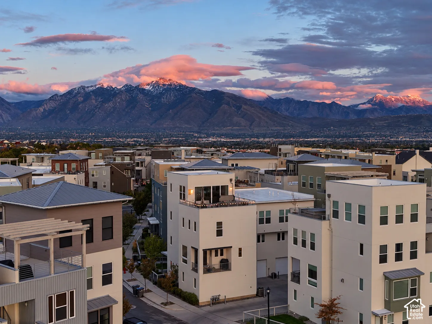 Multi-story residential structures featuring contemporary architectural styling, rooftop terraces, covered balconies, and integrated garage access against a prominent mountain backdrop