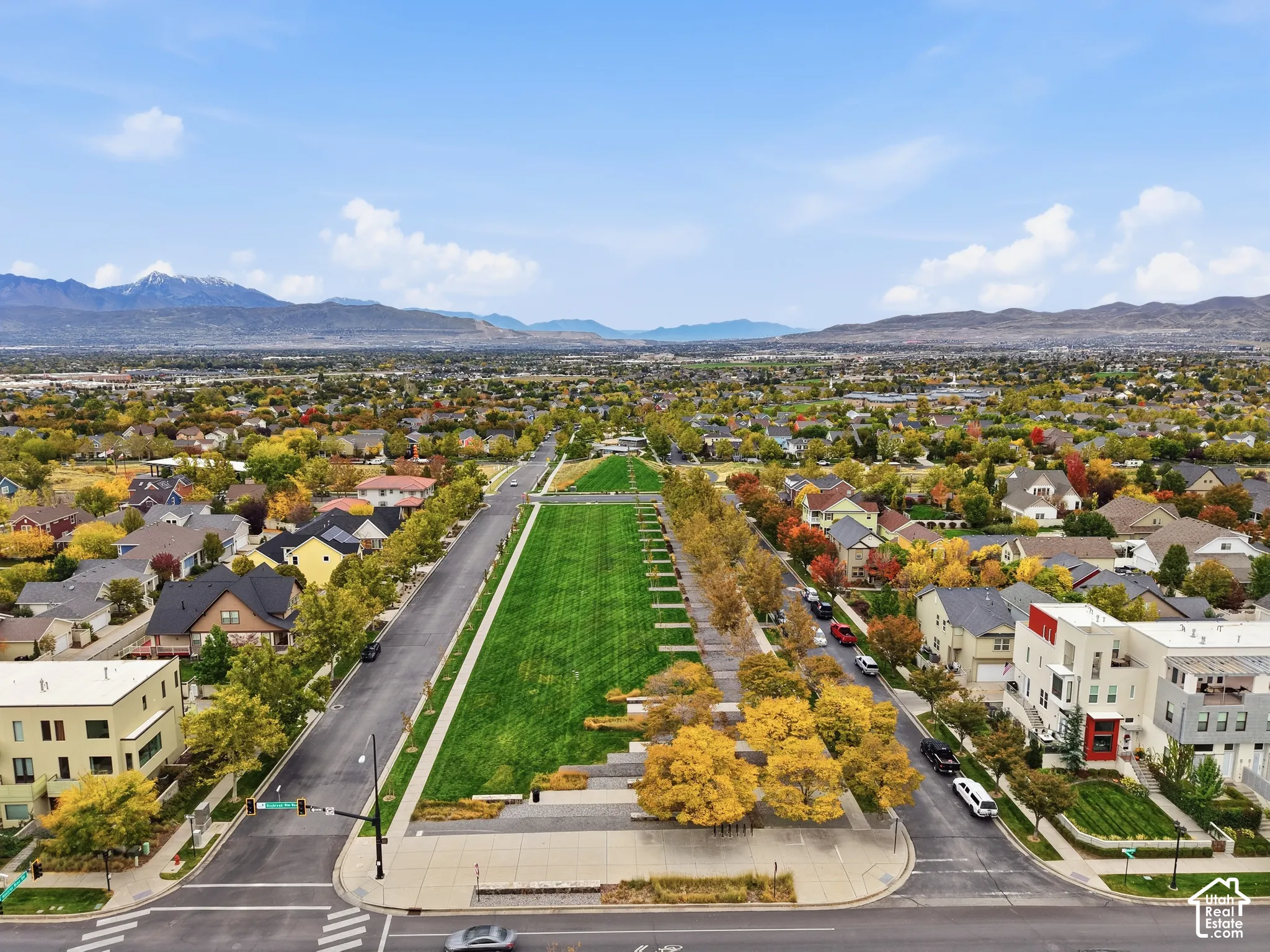 Aerial perspective featuring an elongated central greenbelt, manicured landscaping, mature trees, and a mountain range backdrop