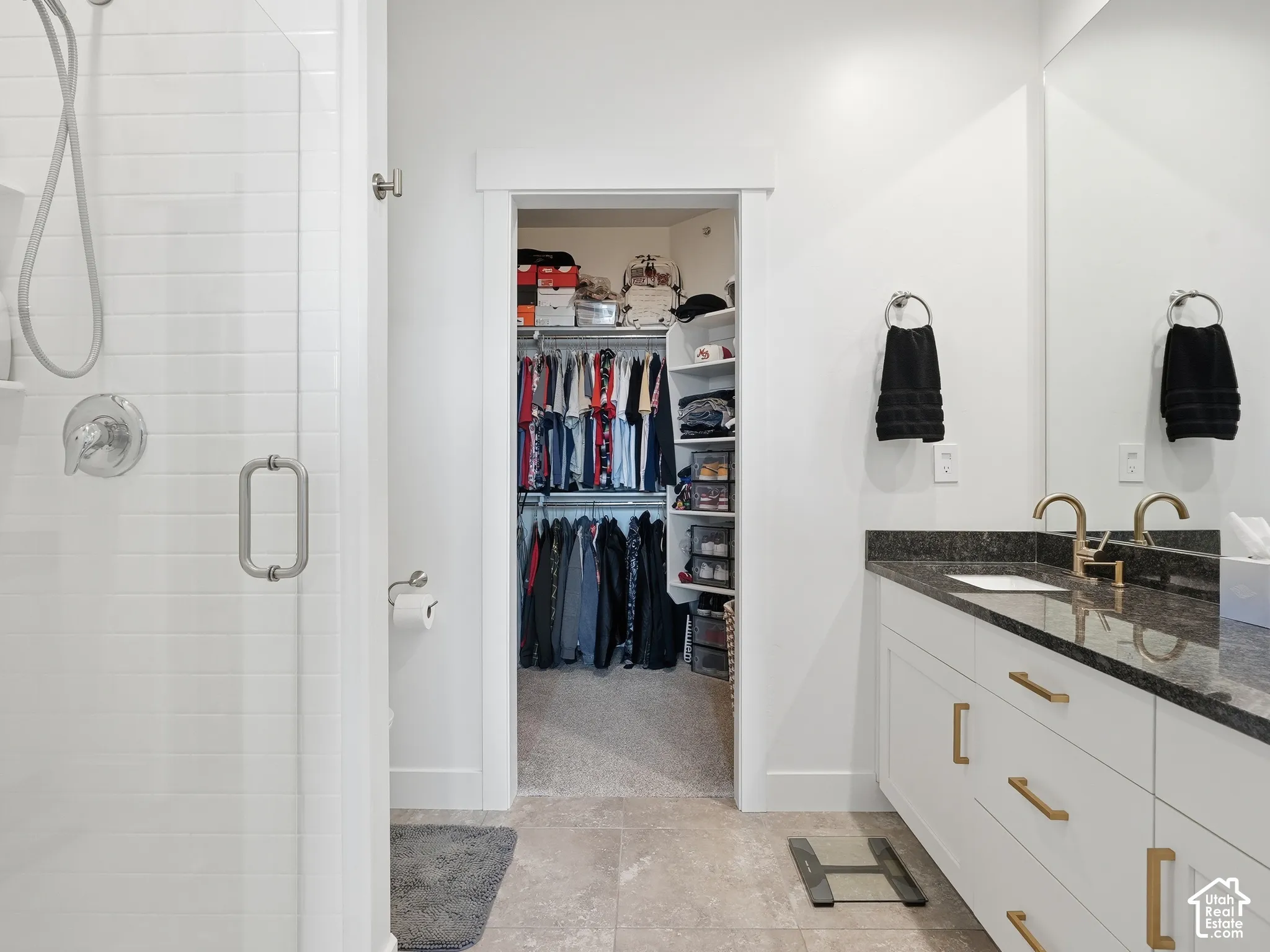 Bathroom featuring a walk-in shower with white subway tile, a white vanity with gold-tone hardware and stone countertop, large wall-mounted mirror, and a walk-in closet with built-in shelving