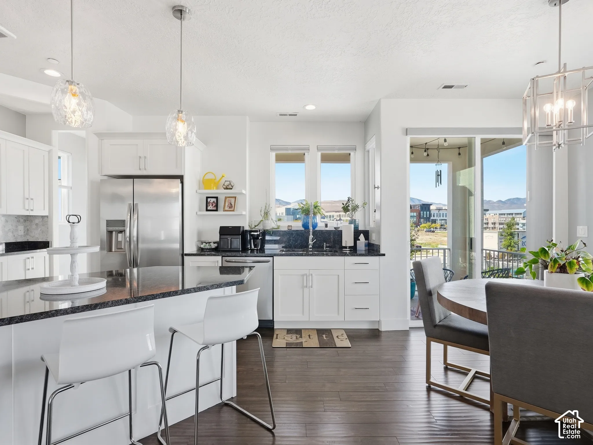 Kitchen featuring white shaker cabinetry, dark stone countertops, stainless steel appliances, wood-finish flooring, and glass pendant lighting