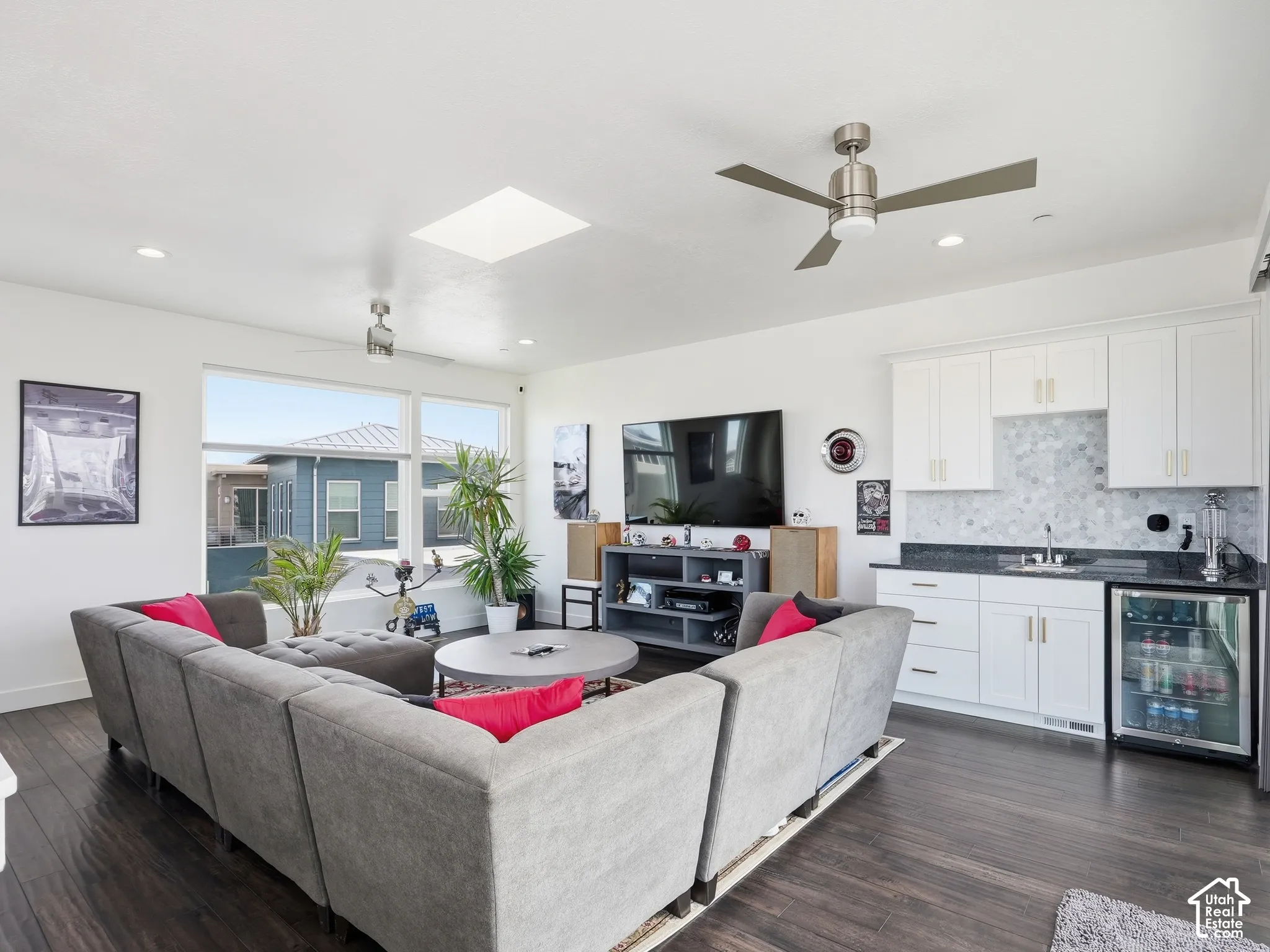 Open living area featuring wood-finish flooring, a built-in wet bar with white cabinetry and dark countertops, a recessed skylight, and dual ceiling fans