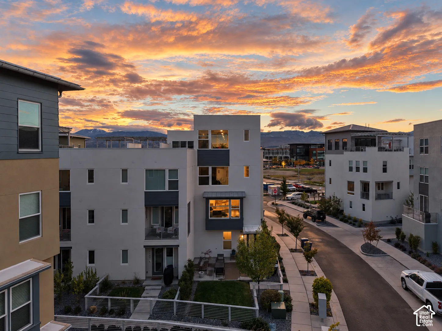 Multi-story residential exteriors featuring stucco facades, metal roofing accents, recessed balconies, and private ground-level patio spaces against a mountain backdrop