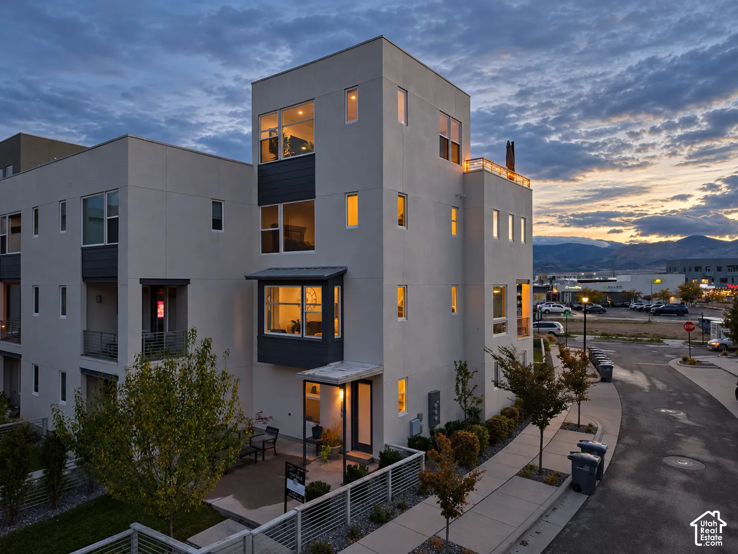Contemporary multi-story exterior featuring smooth stucco siding, a rooftop terrace with metal railing, a cantilevered bay window, and large multi-pane windows set against a mountain backdrop