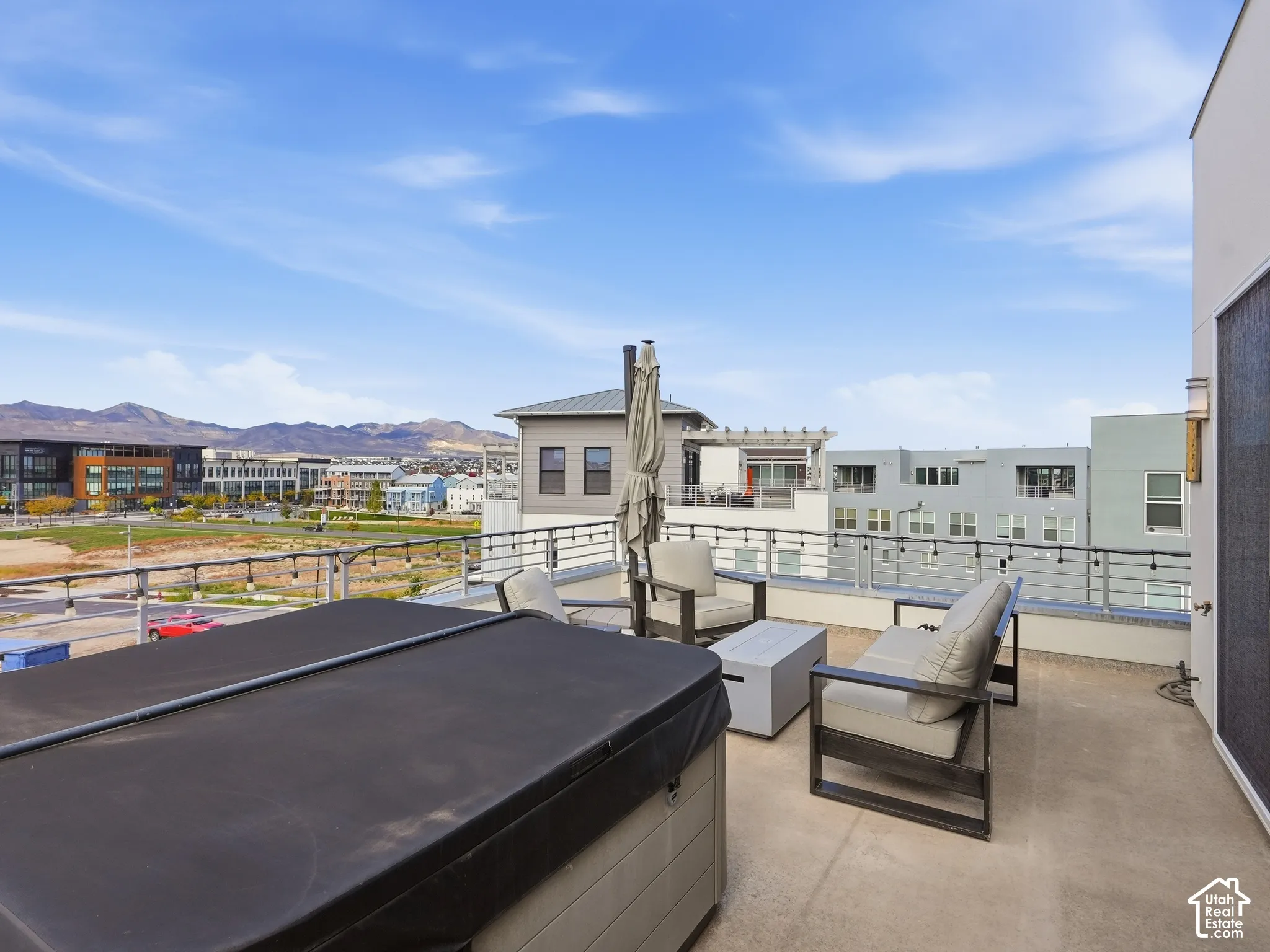 Rooftop terrace featuring a hot tub, metal railing, string lighting, and mountain backdrop