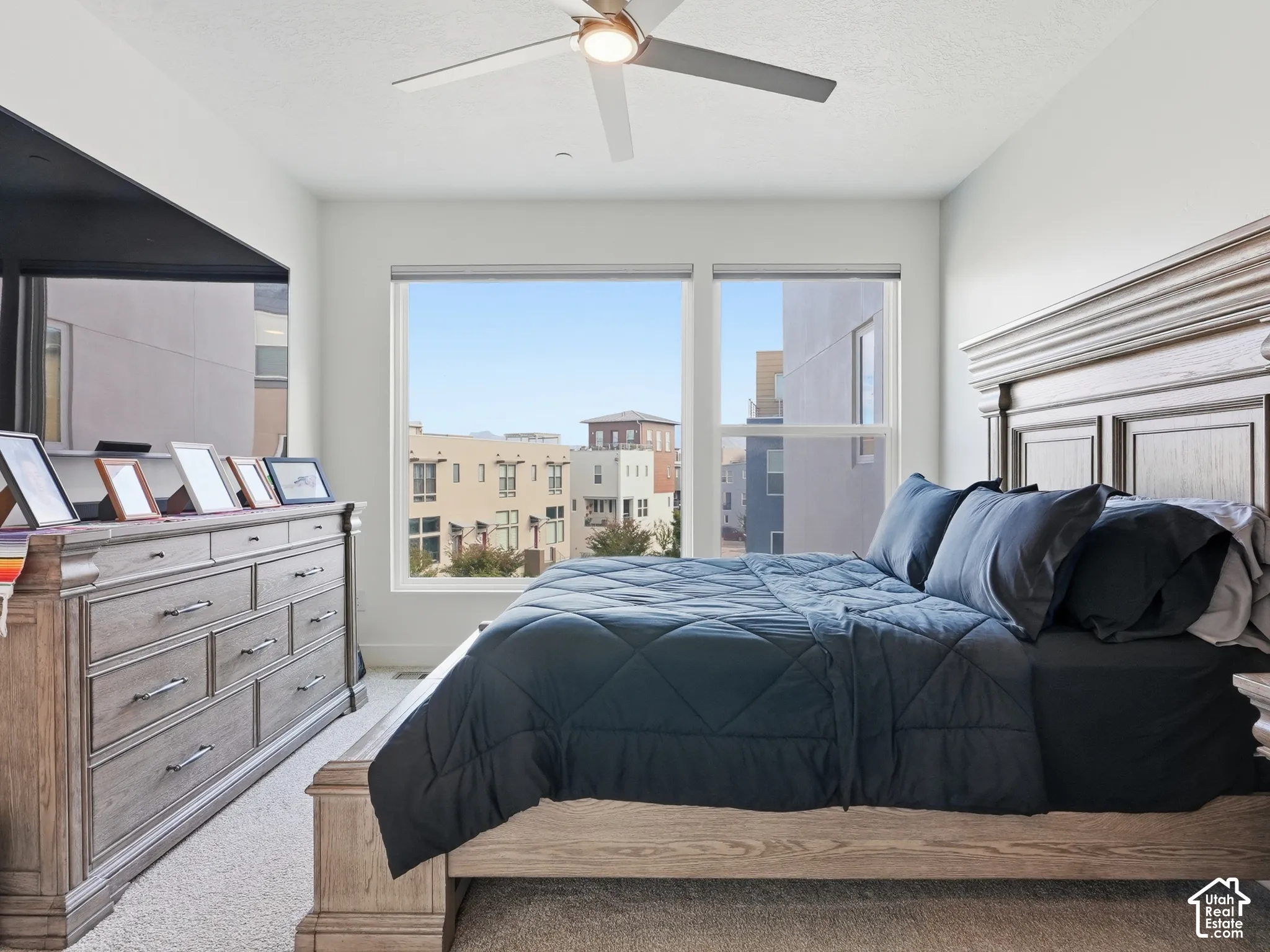 Bedroom featuring neutral carpet flooring, large picture windows, and a ceiling-mounted light fixture with fan
