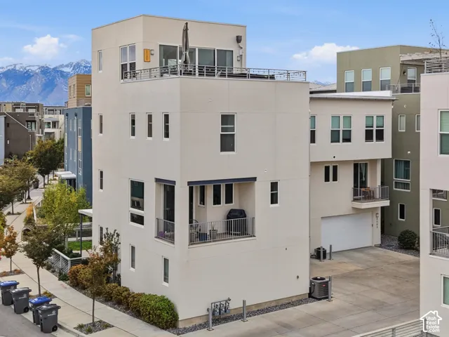 Contemporary multi-story exterior with a rooftop deck, second-story covered balcony, stucco siding, and mountain backdrop