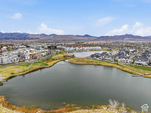 Aerial perspective showcasing a community lake, paved walking paths, landscaped green space, and a mountainous backdrop