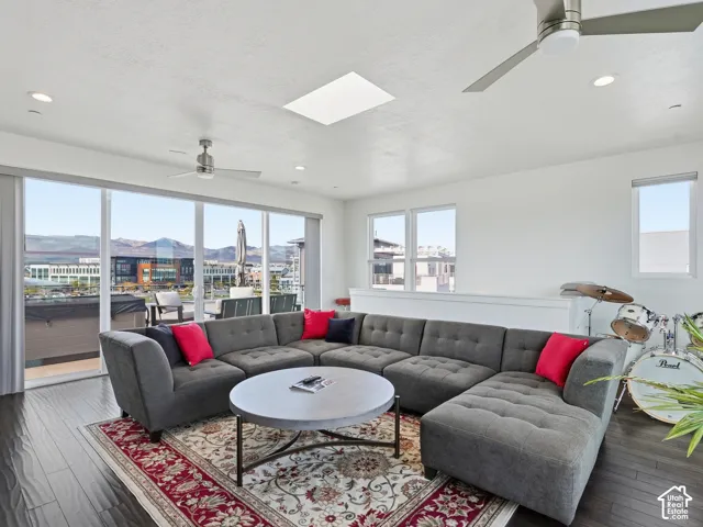 Living area featuring wood-finish flooring, a ceiling-mounted skylight, recessed lighting, dual ceiling fans, and expansive floor-to-ceiling glass sliding doors