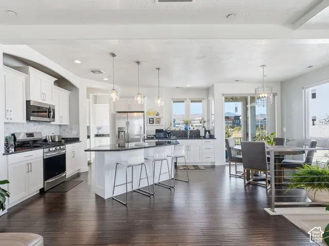 Kitchen featuring white shaker-style cabinetry, dark stone countertops, stainless steel appliances, a center island with pendant lighting, and wood-finish flooring