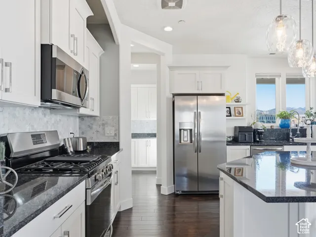 Kitchen featuring white cabinetry, dark stone countertops, stainless steel appliances, decorative glass pendant lighting, and wood-finish flooring
